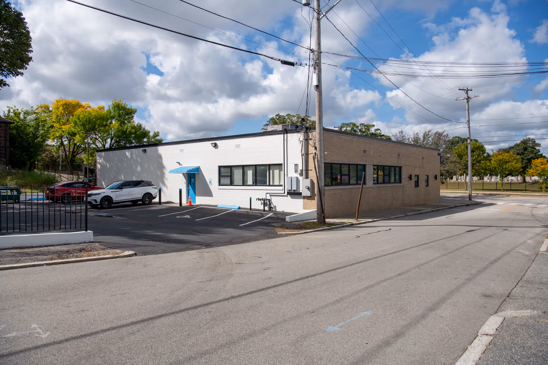 Single-story building with white and beige exterior, parking lot, and visible power lines.