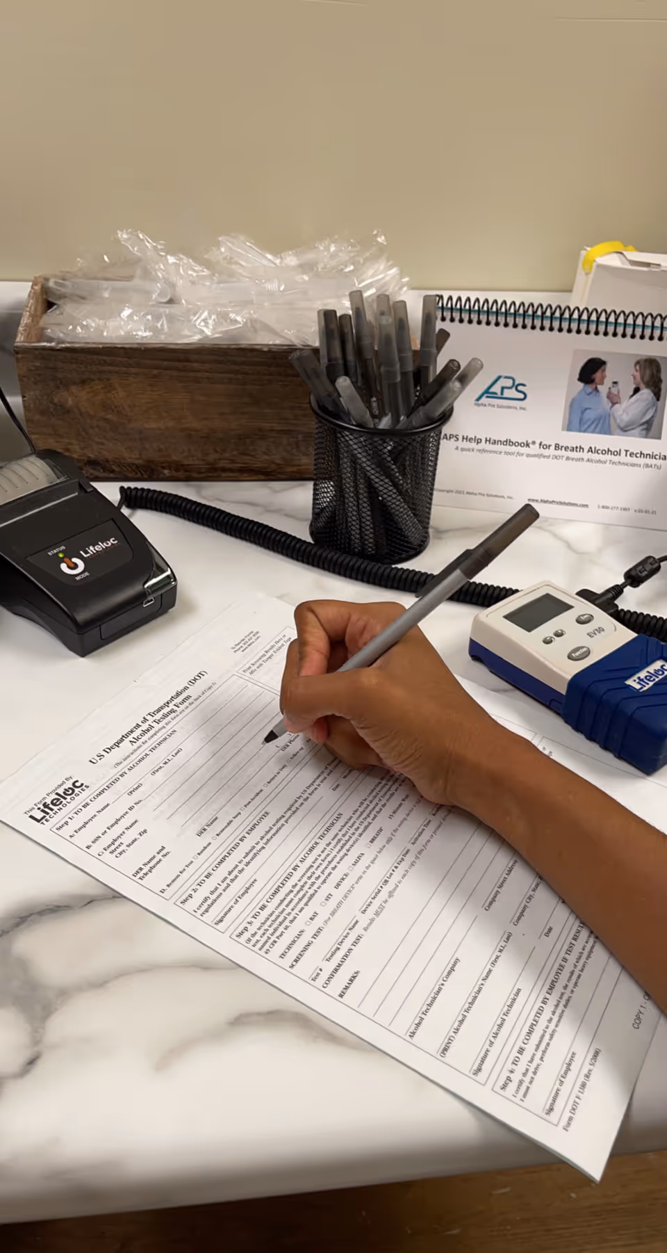 A hand writes on a form at a marble desk with medical devices nearby.