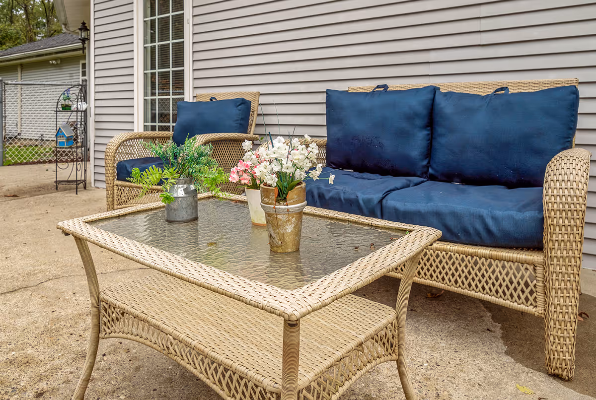 Wicker outdoor seating with blue cushions and potted flowers on a concrete patio.