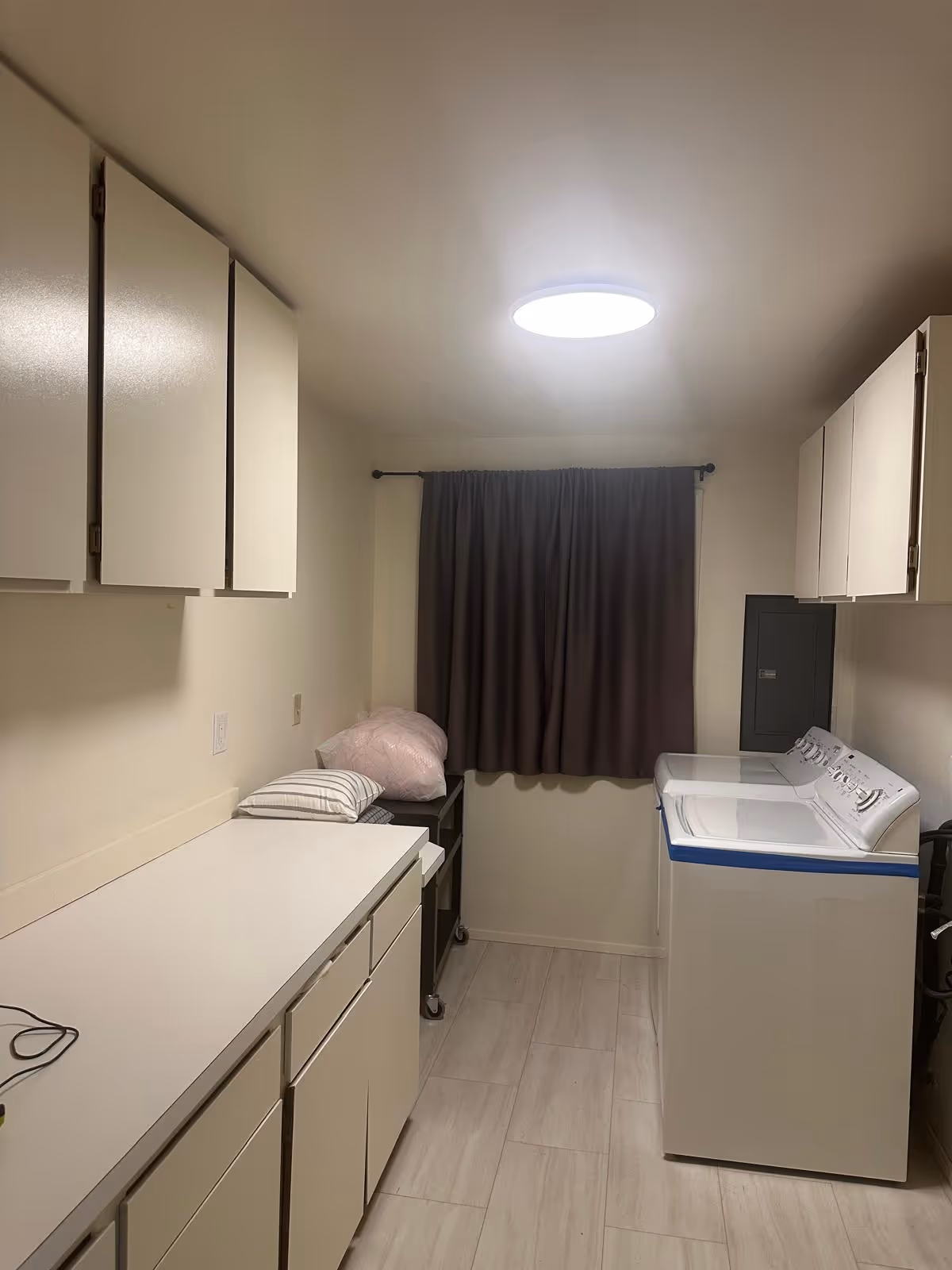 Laundry room in a senior living facility with washer, cabinets, and a curtain.