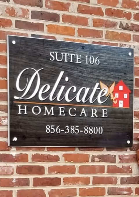 Sign reading Delicate Homecare Suite 106 with a house logo on a brick wall.