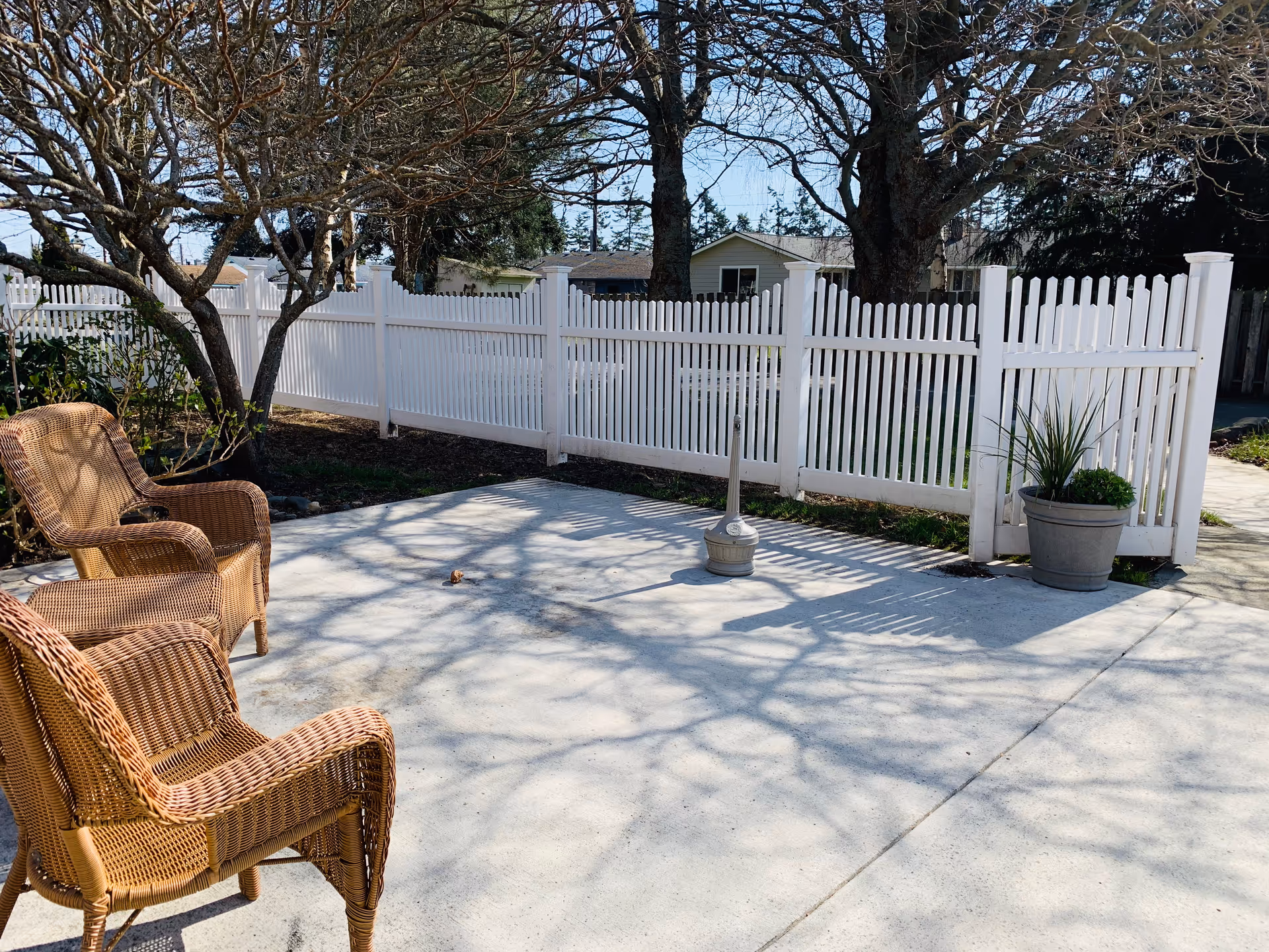 Outdoor patio with wicker chairs, a white picket fence, and potted plants.