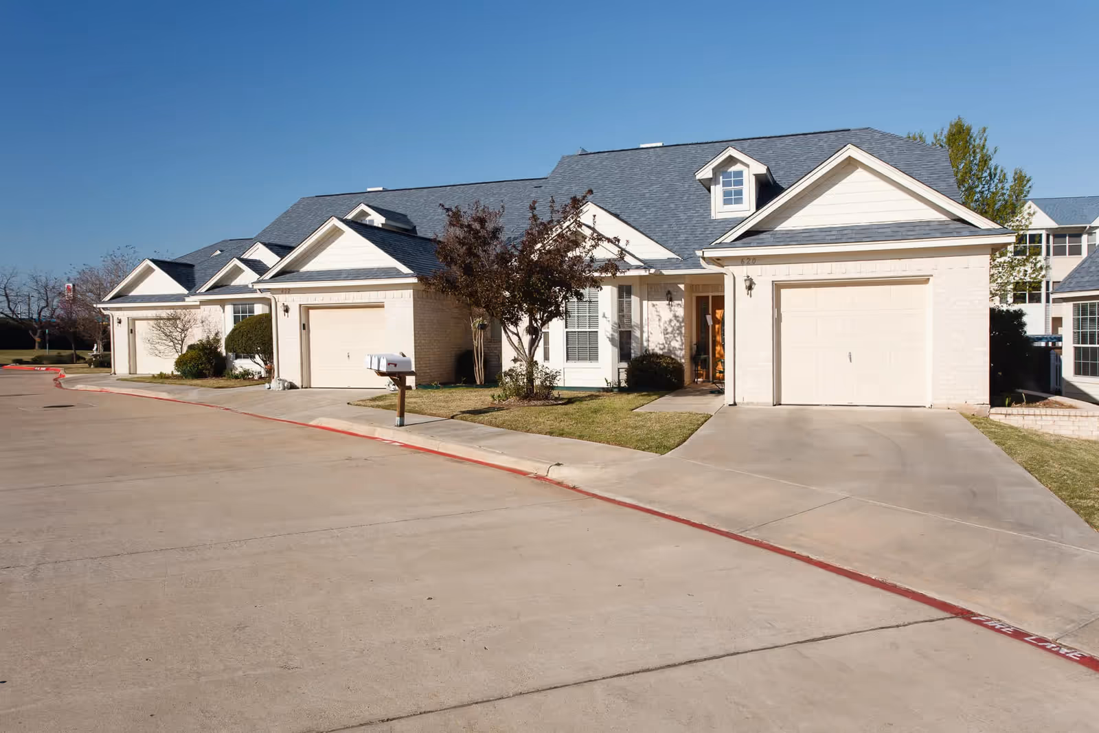 Row of attached, light-brick senior living homes with garages and a curved driveway.