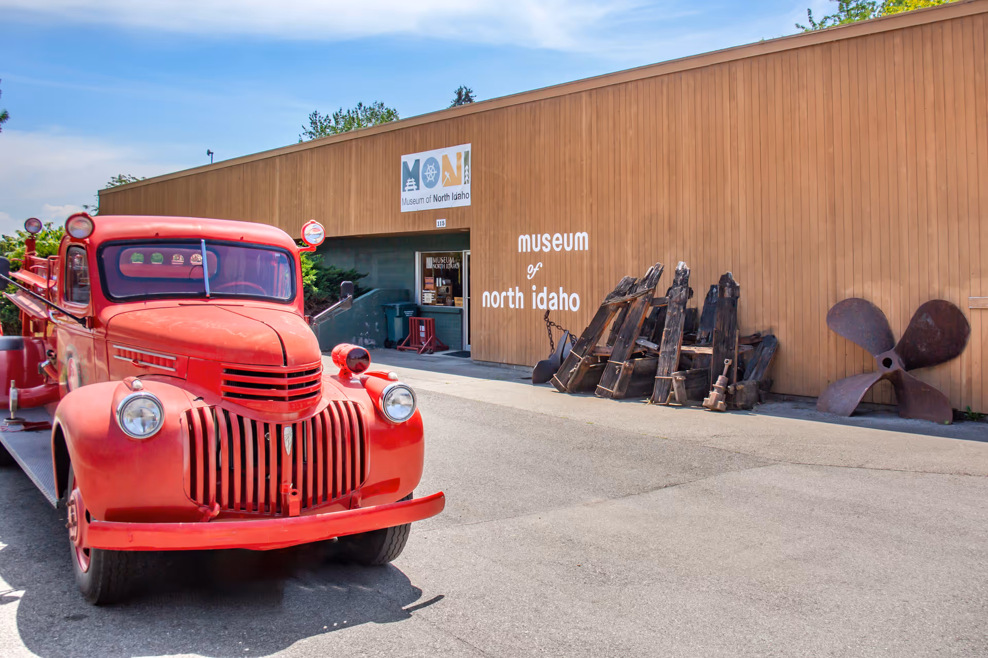 Red vintage truck parked outside the Museum of North Idaho with old farm equipment.