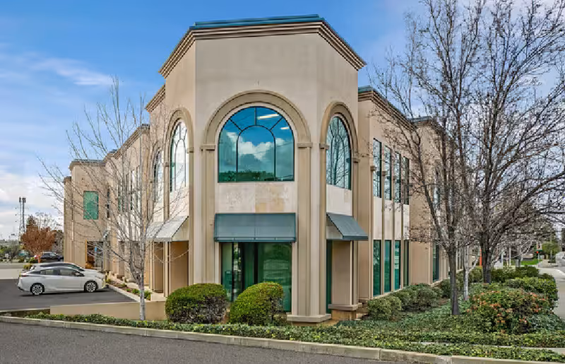Exterior view of a beige senior living building with arched windows and landscaped shrubs.