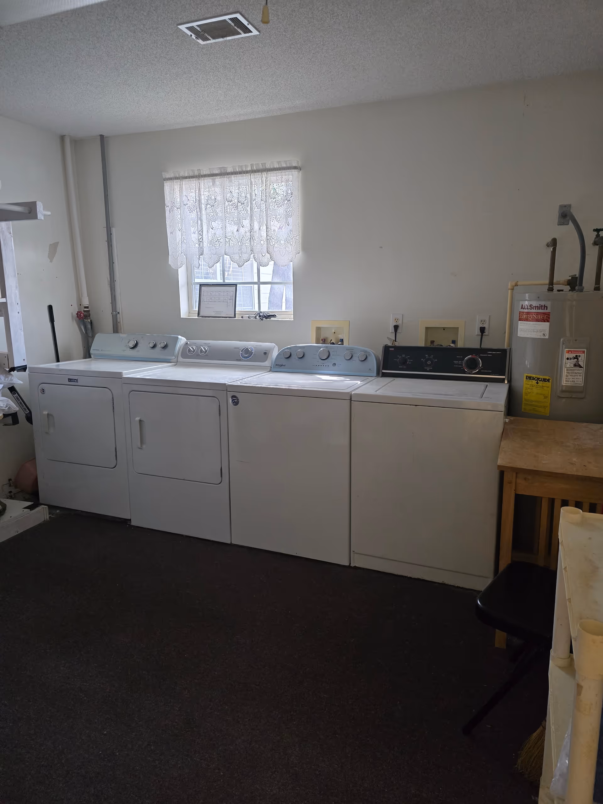 Row of top-loading washing machines and a dryer in a small laundry room.