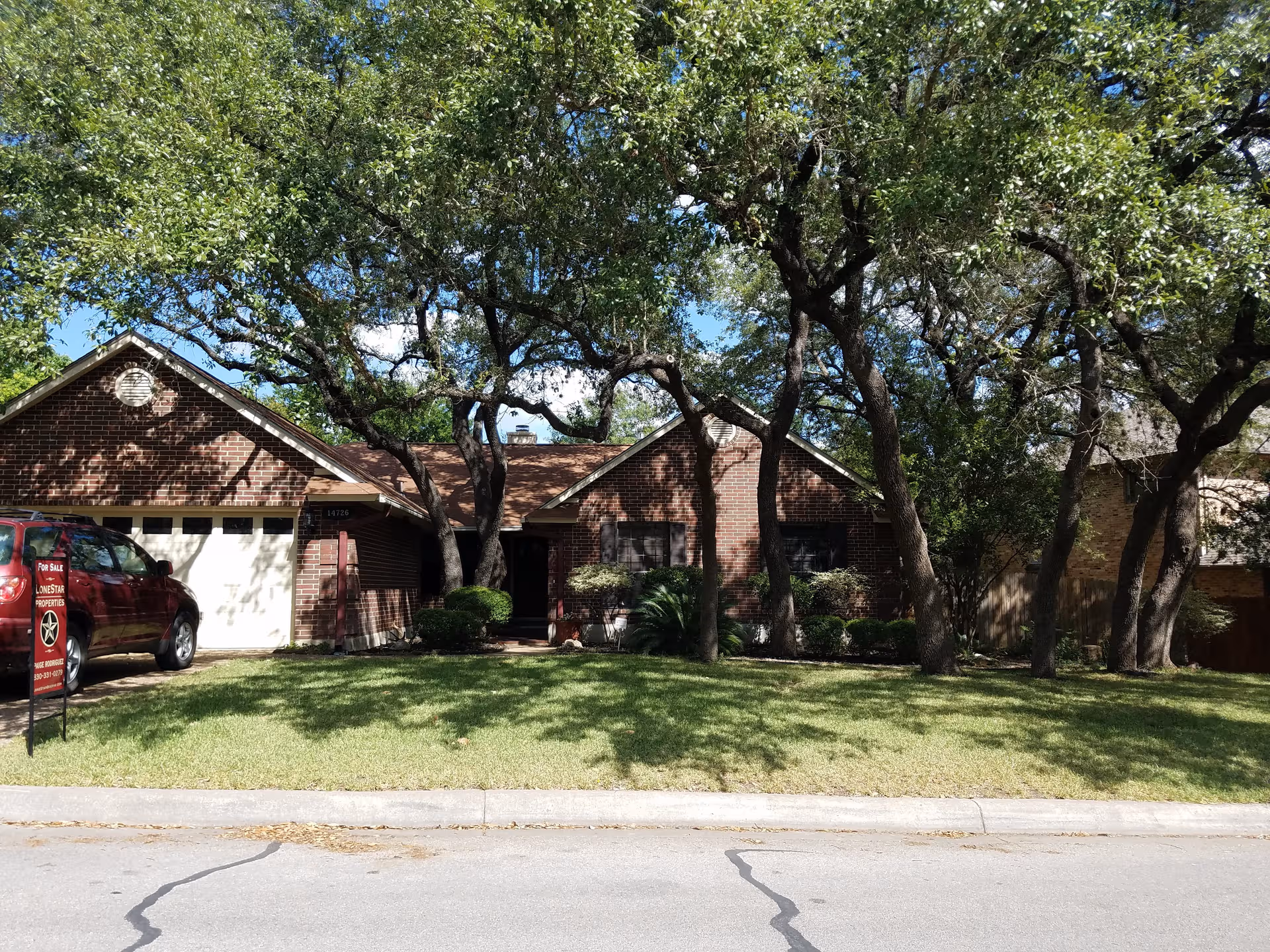 Brick single-story building with large trees and a front lawn beside the street.