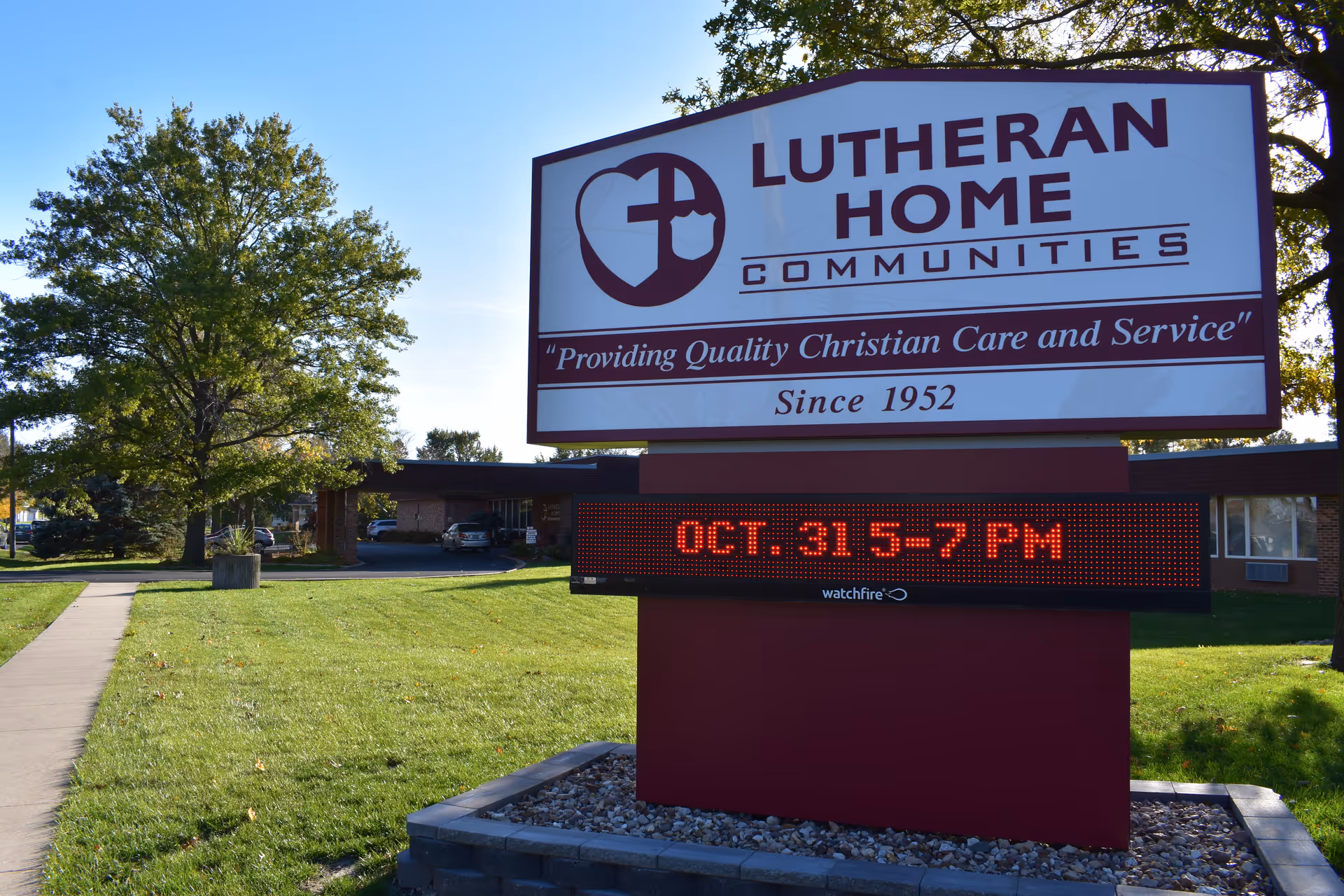 Outdoor scene with Lutheran Home Communities sign on a grassy lawn and building behind.