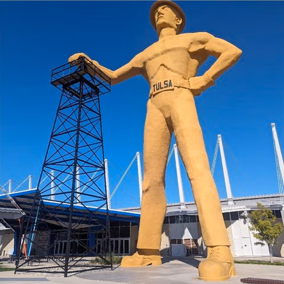 Large golden statue of a muscular man with hands on hips beside a metal framework.