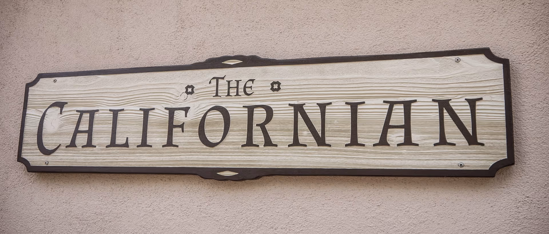 A beige exterior wall with a wooden sign reading The Californian.
