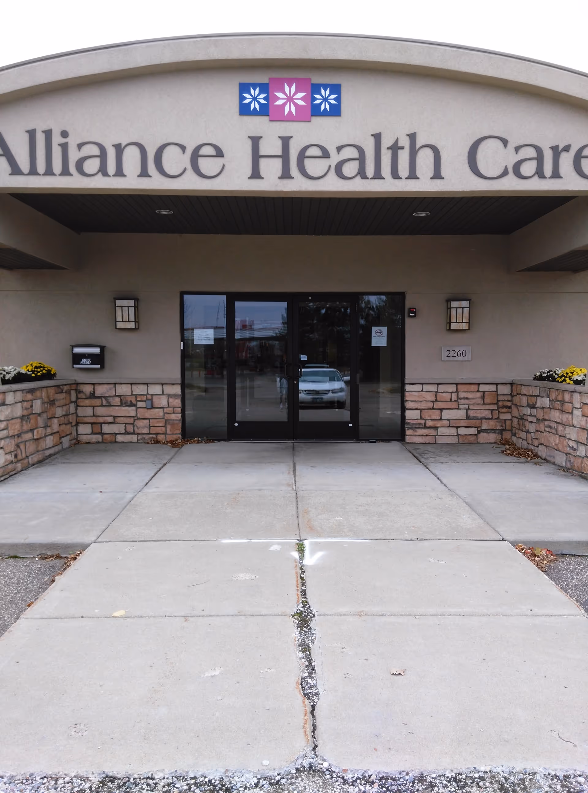 Front entrance of Alliance Health Care facility with glass doors and stone accent walls.