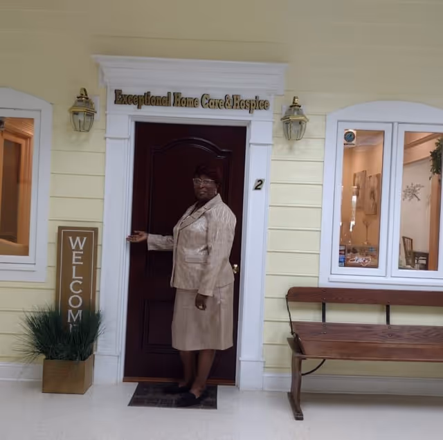 A woman stands at the entrance of a yellow building labeled Exceptional Home Care & Hospice.