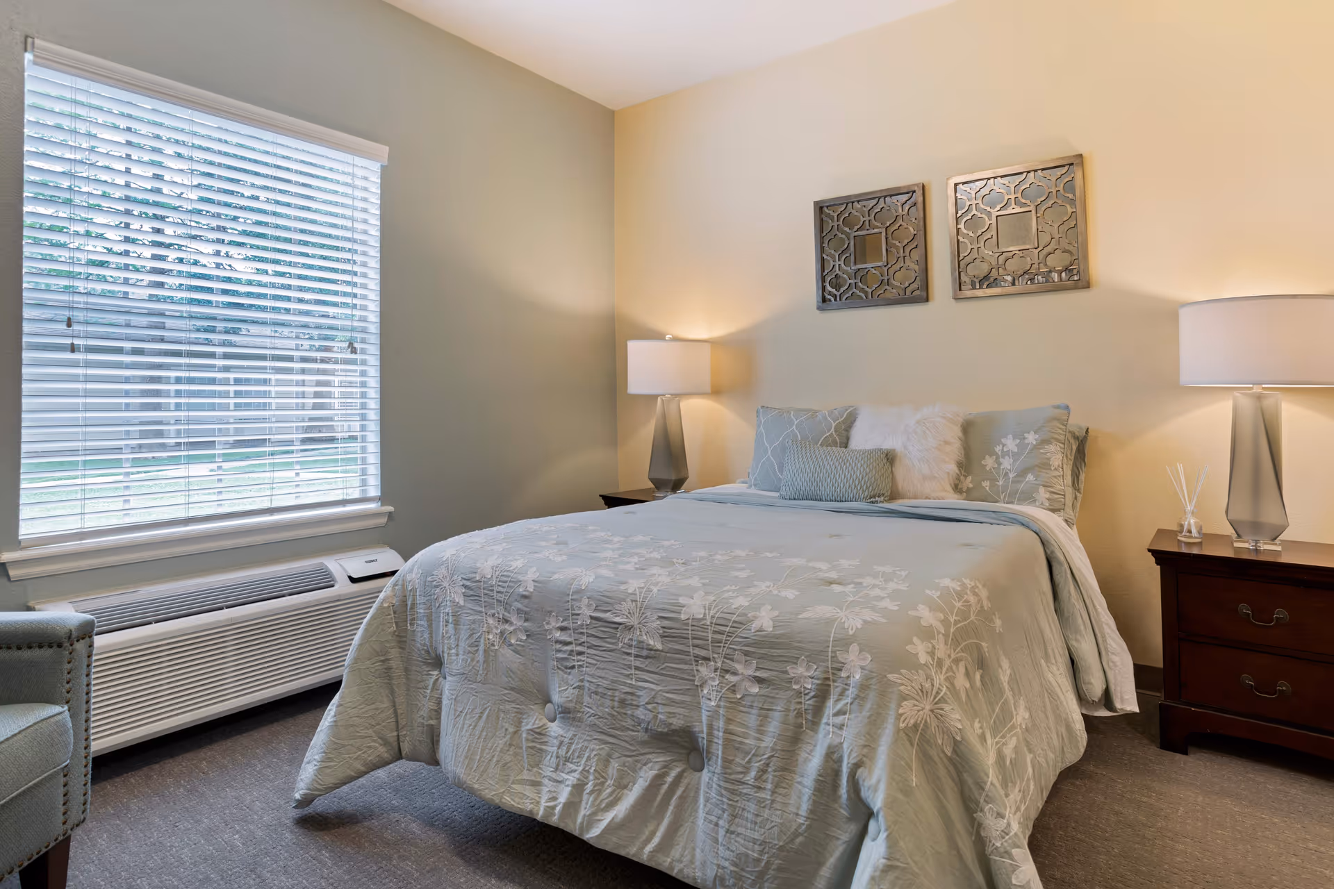 A well-lit senior living bedroom with a blue floral bedspread and nightstands.