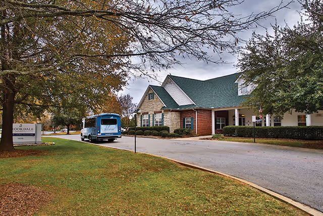 Exterior view of Royal Adult Family Home with driveway, greenery, and a blue shuttle bus.