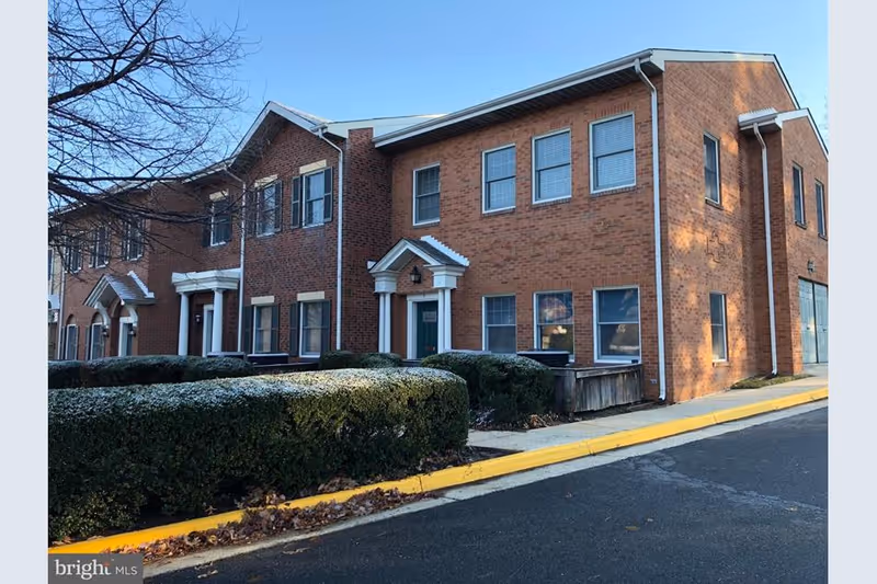 Brick senior living facility exterior with hedges, sidewalk, and a yellow curb.