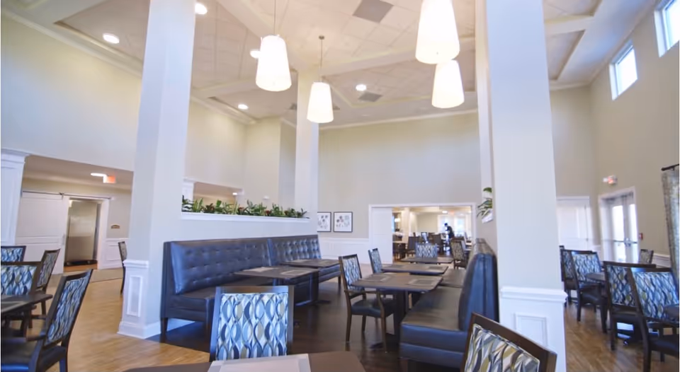 Bright dining hall with seating booths, tables, and pendant lights in a spacious senior living facility.