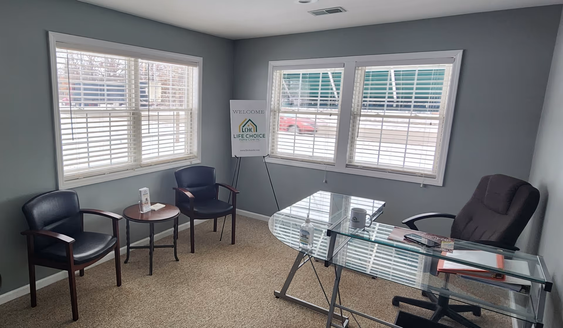 A small waiting area with a glass desk, four chairs, and a Life Choice welcome sign.