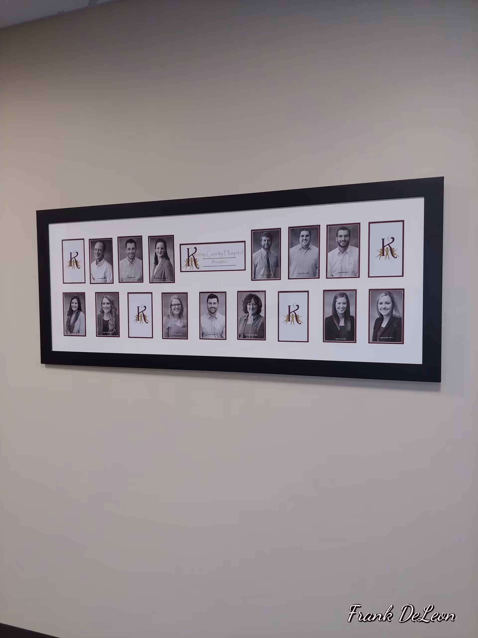 Long framed collage of black-and-white staff portraits mounted on a beige hallway wall.