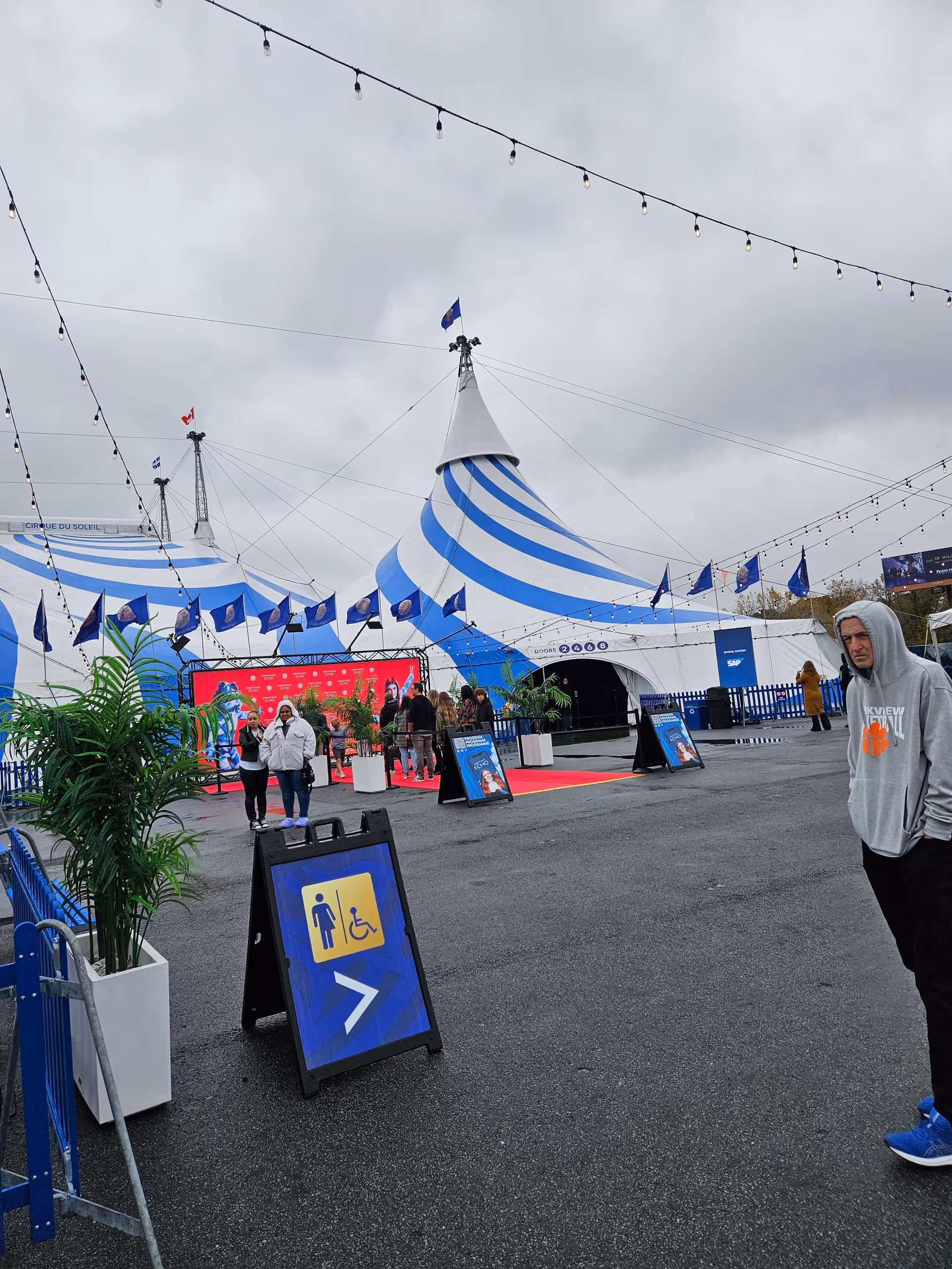 Outdoor area with blue-and-white striped tents, string lights, and people walking.