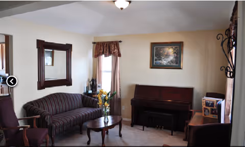 A cozy living room with striped sofa, chairs, coffee table, piano, mirror, and window.