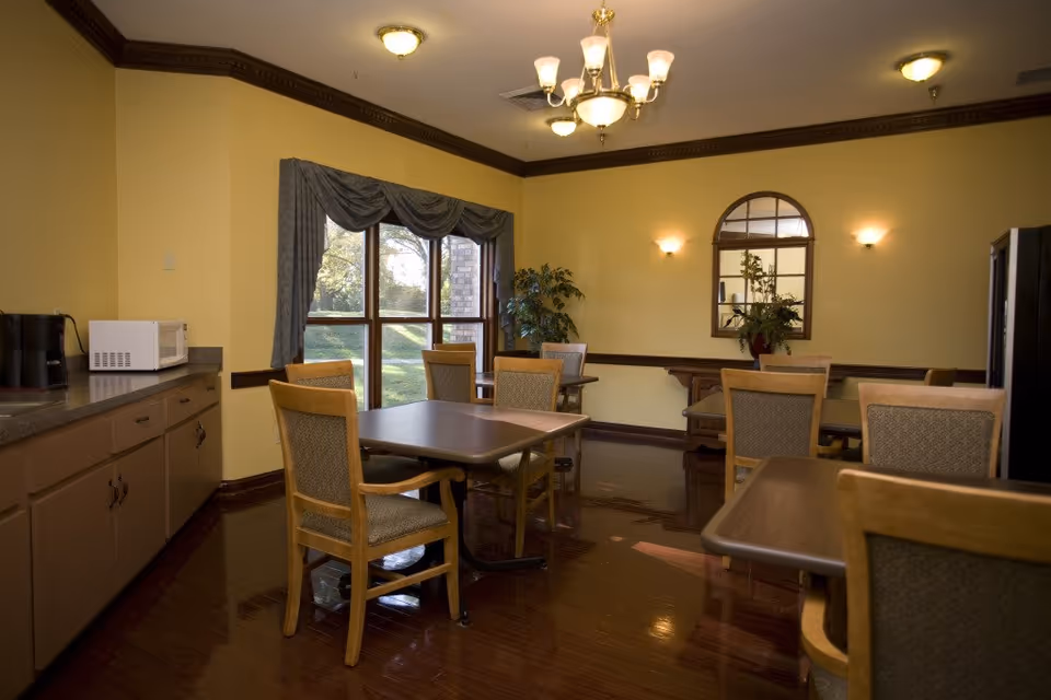 Interior dining room with tables, chairs, windows, and kitchenette on the left.