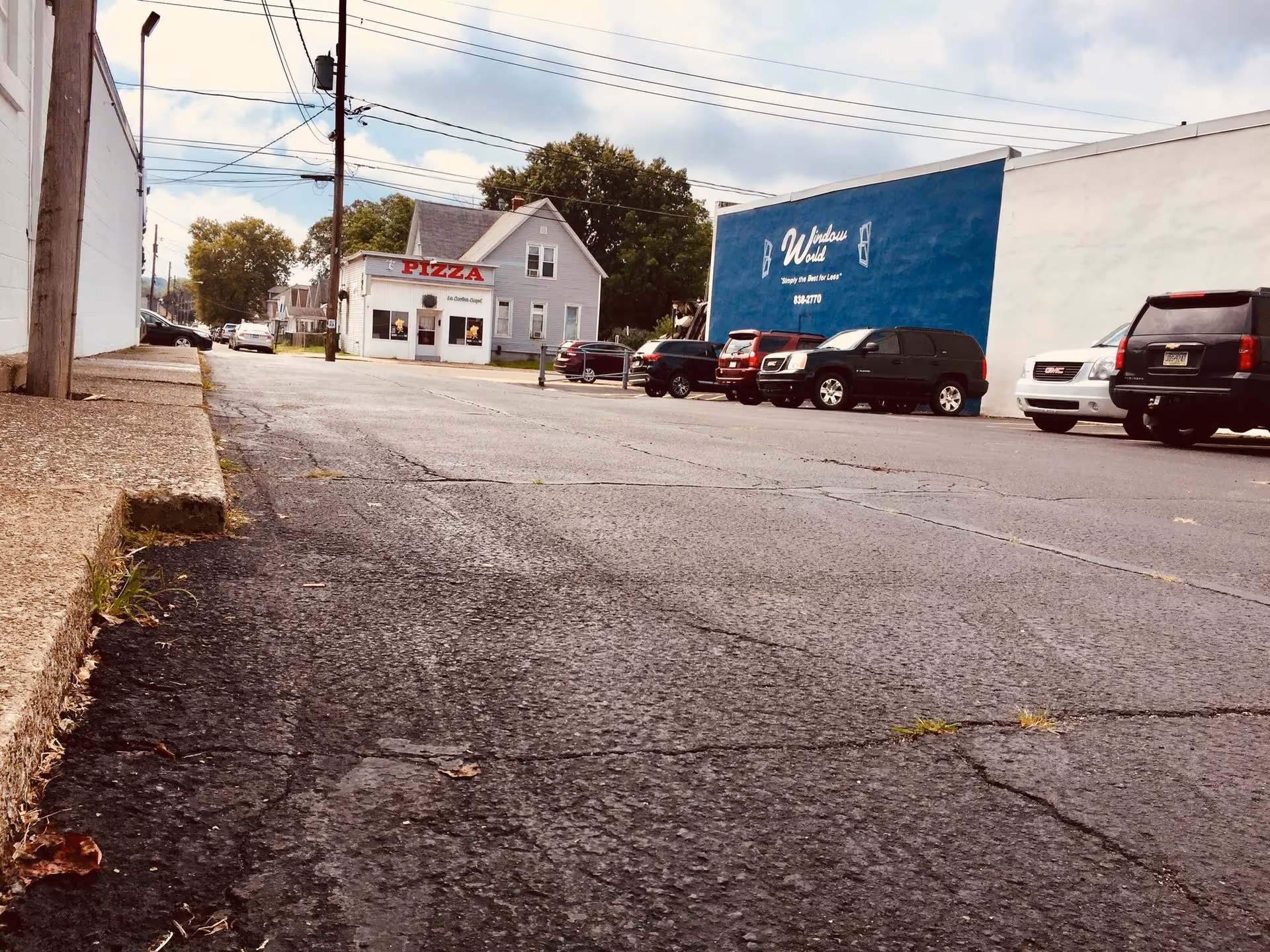 Exterior street view with parked cars, a pizza shop, and a blue building.