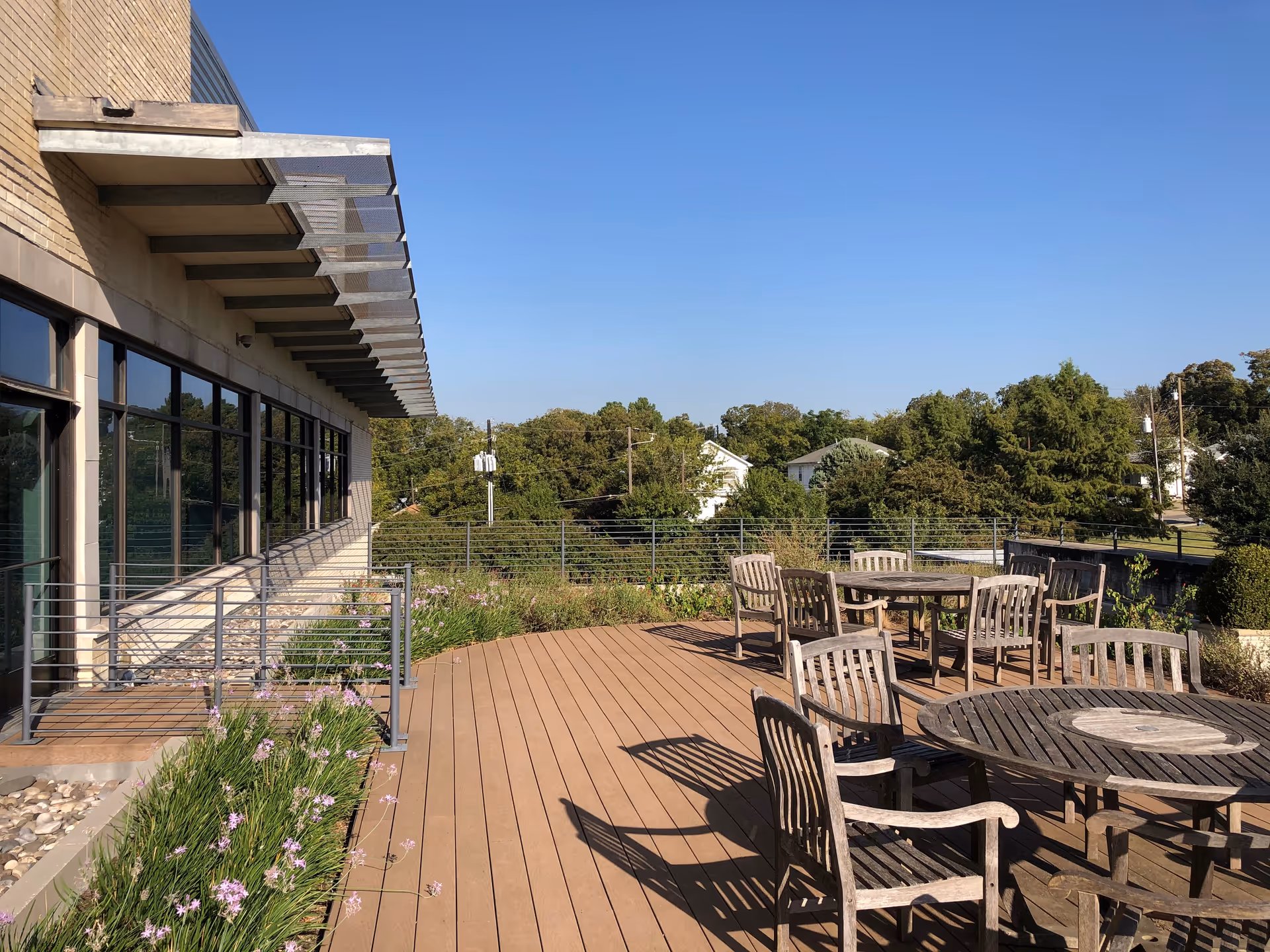 Outdoor wooden deck with tables and chairs beside a glass-front facility.