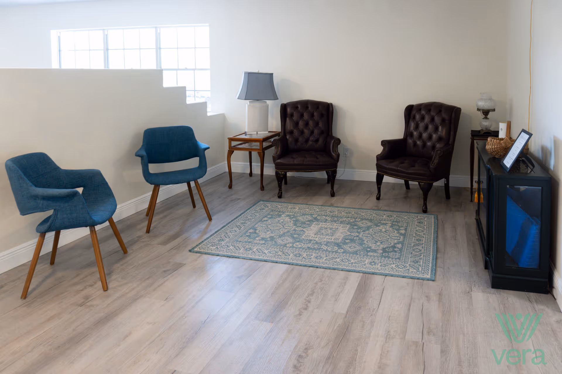 A quiet lounge area with blue chairs, brown leather armchairs, a rug, and a TV cabinet.