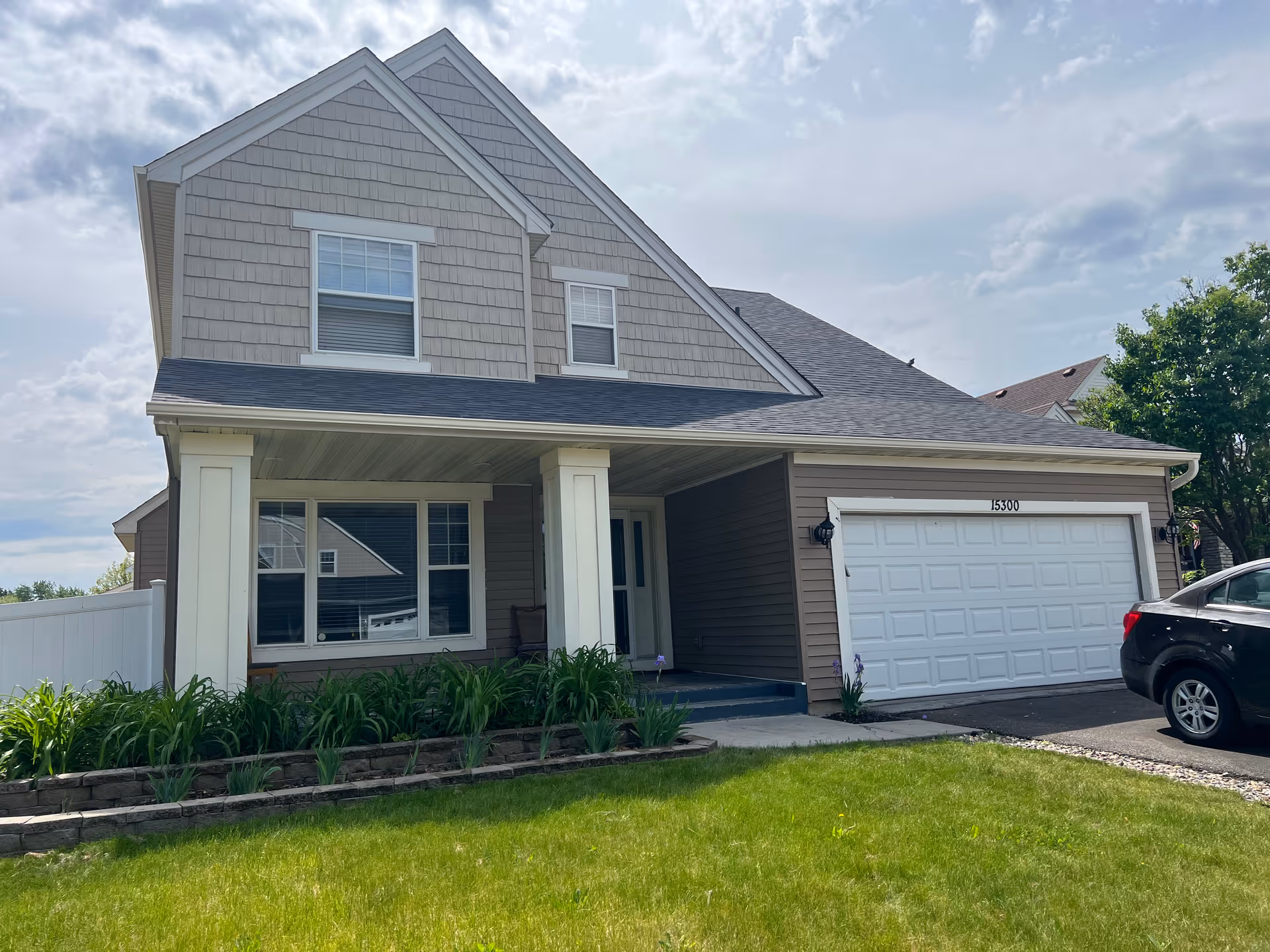 Suburban two-story house with front porch, attached garage, and well-kept lawn