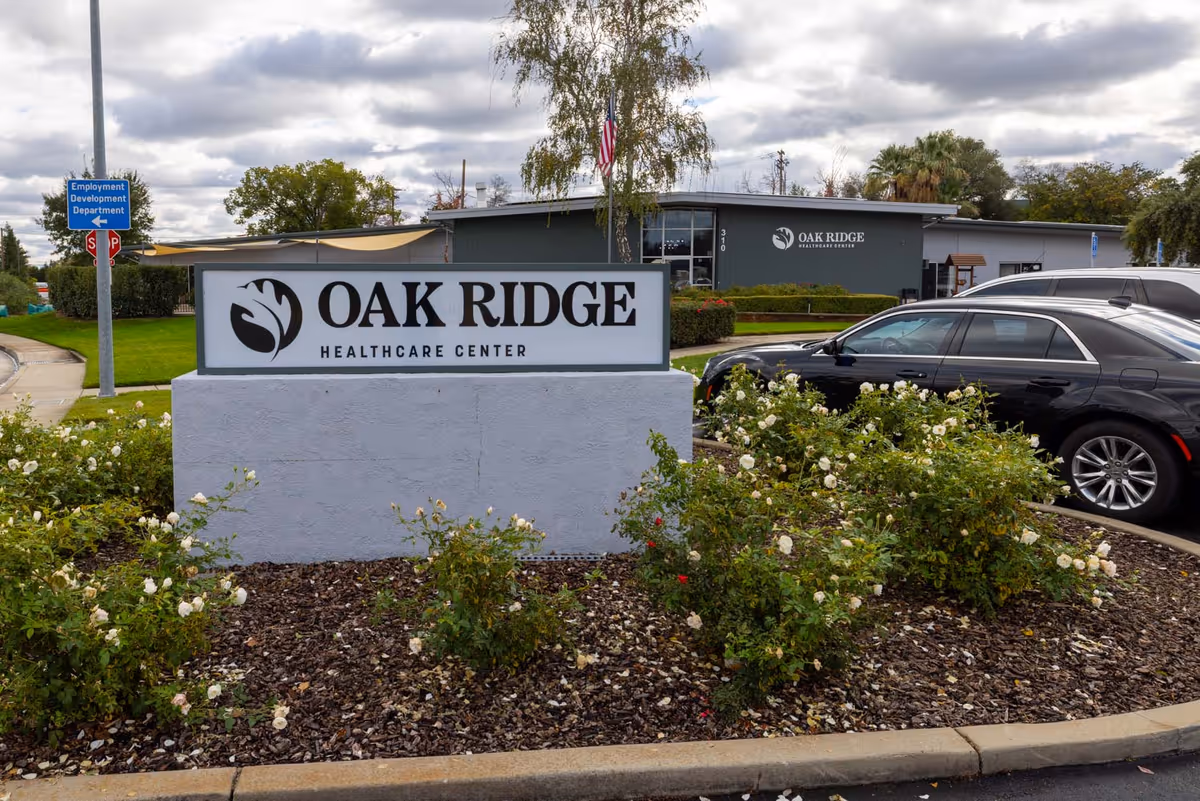 Oak Ridge Healthcare Center sign with landscaped roses and parked cars in front.