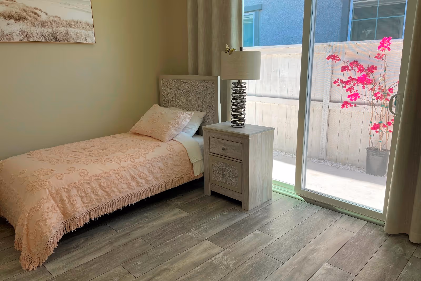 Single bed with pastel bedspread, nightstand, lamp, and sliding glass door to a patio.
