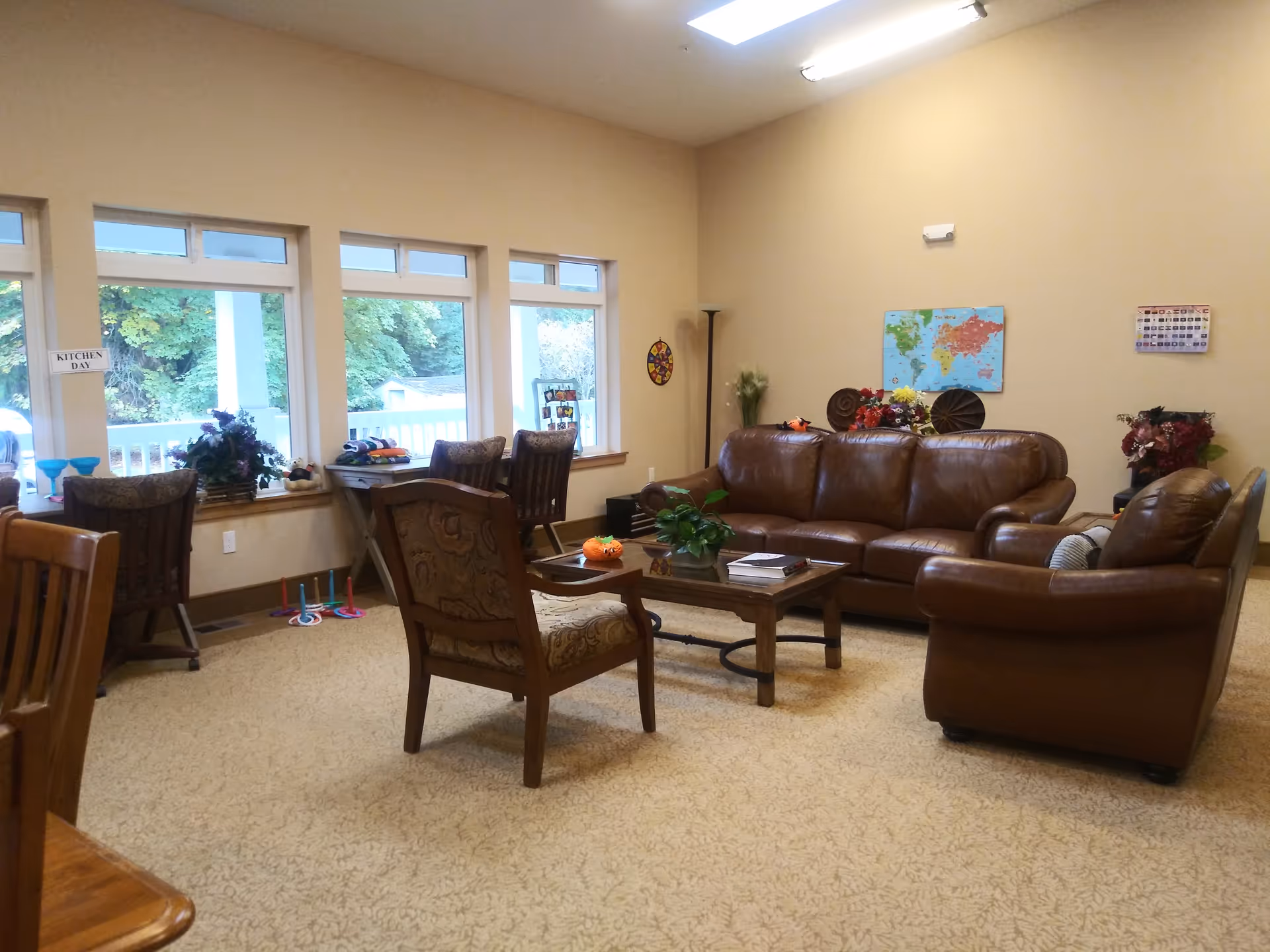 Cozy senior living lounge with brown leather sofas, chairs, a coffee table, and large windows.