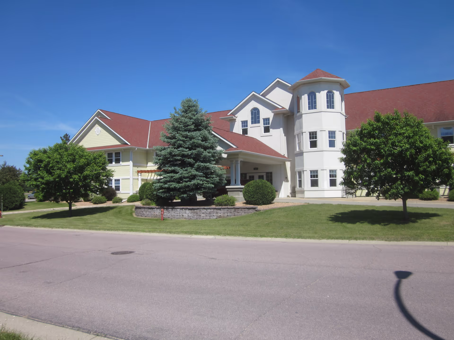 Senior living facility building with red roof, white exterior, and landscaped front yard.