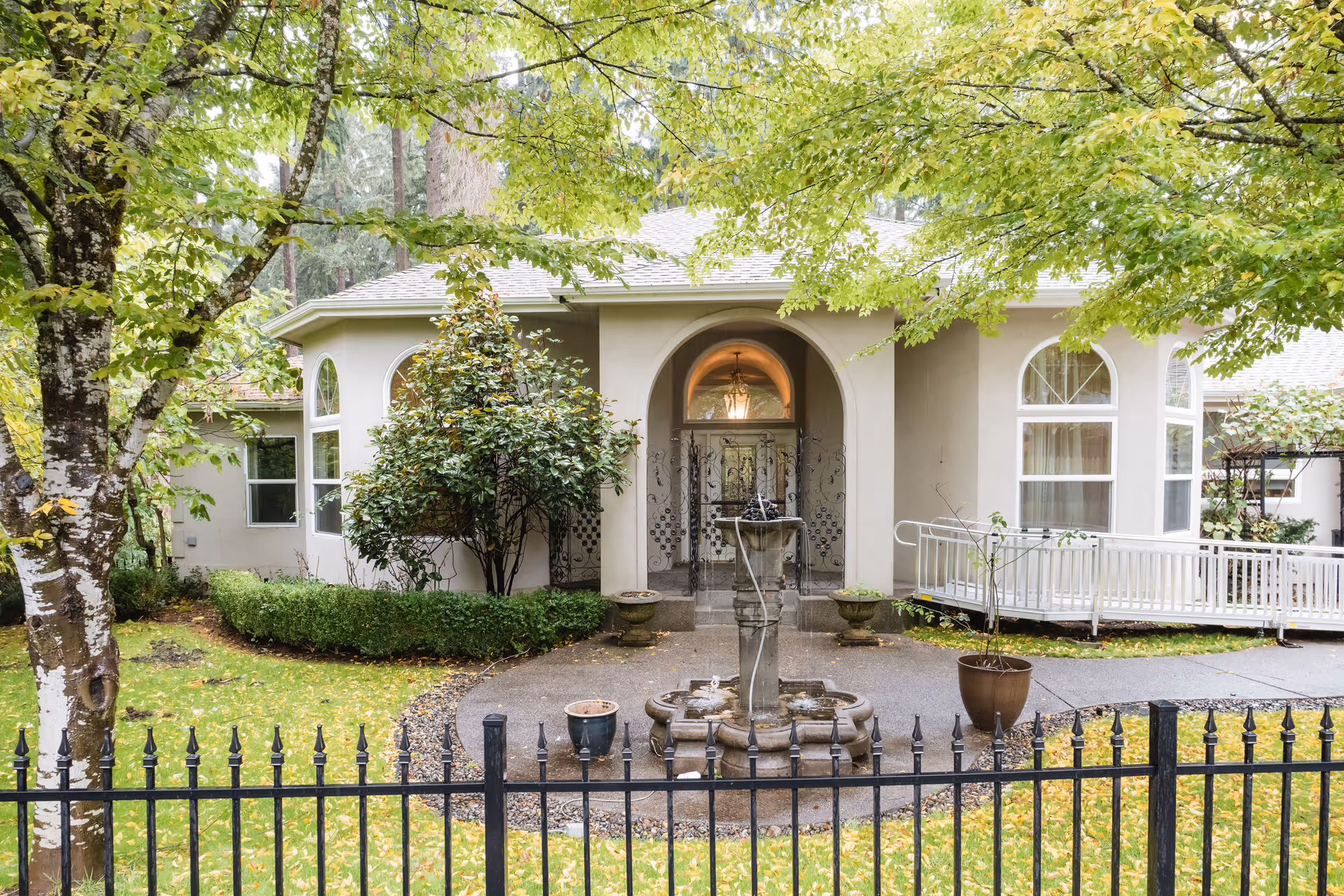 Front facade of Lakewood Seniors AFH with arched entry, fountain, and lush greenery.