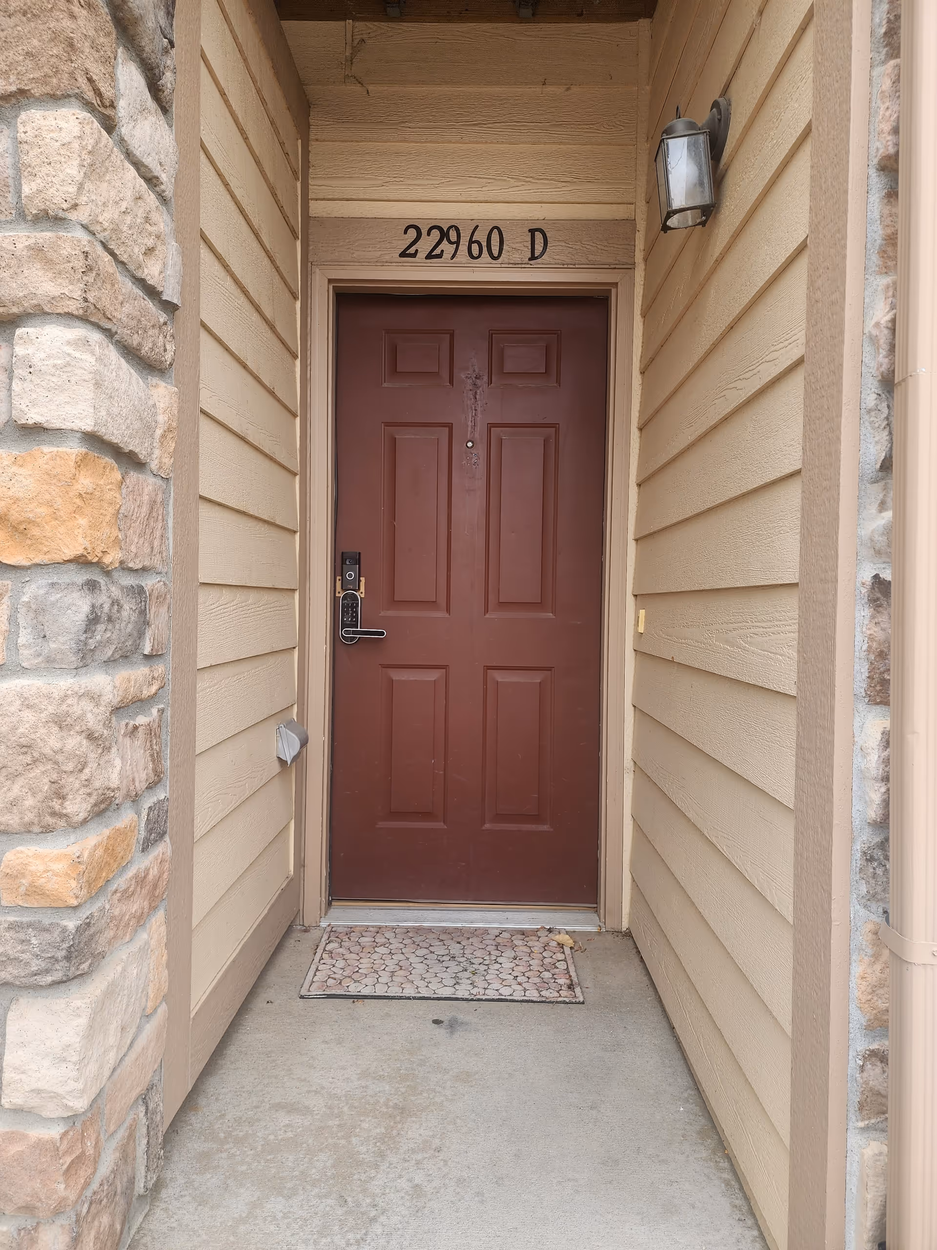 Front exterior entry with beige siding, stone wall, and door marked 22960 D.