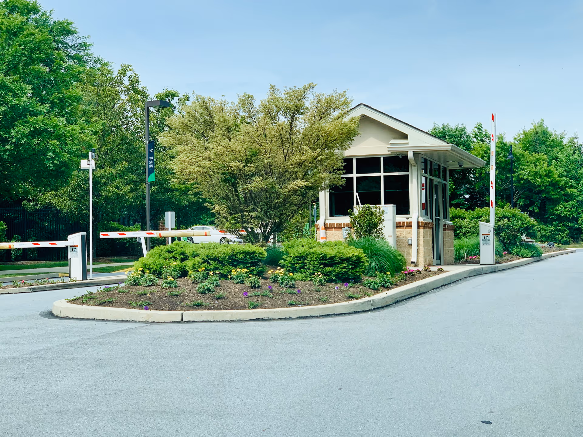 Exterior view of a gated entrance with a guardhouse and landscaped island.