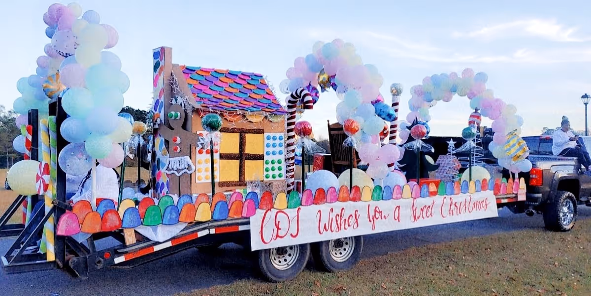Colorful candy-themed parade float with balloons on a trailer outdoors.