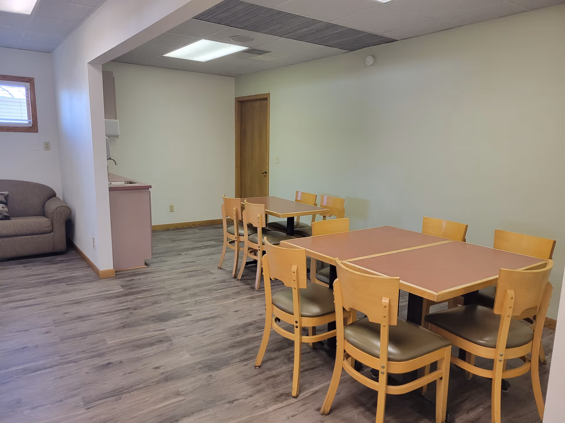 Bright dining room with wooden tables and chairs in a senior care facility.