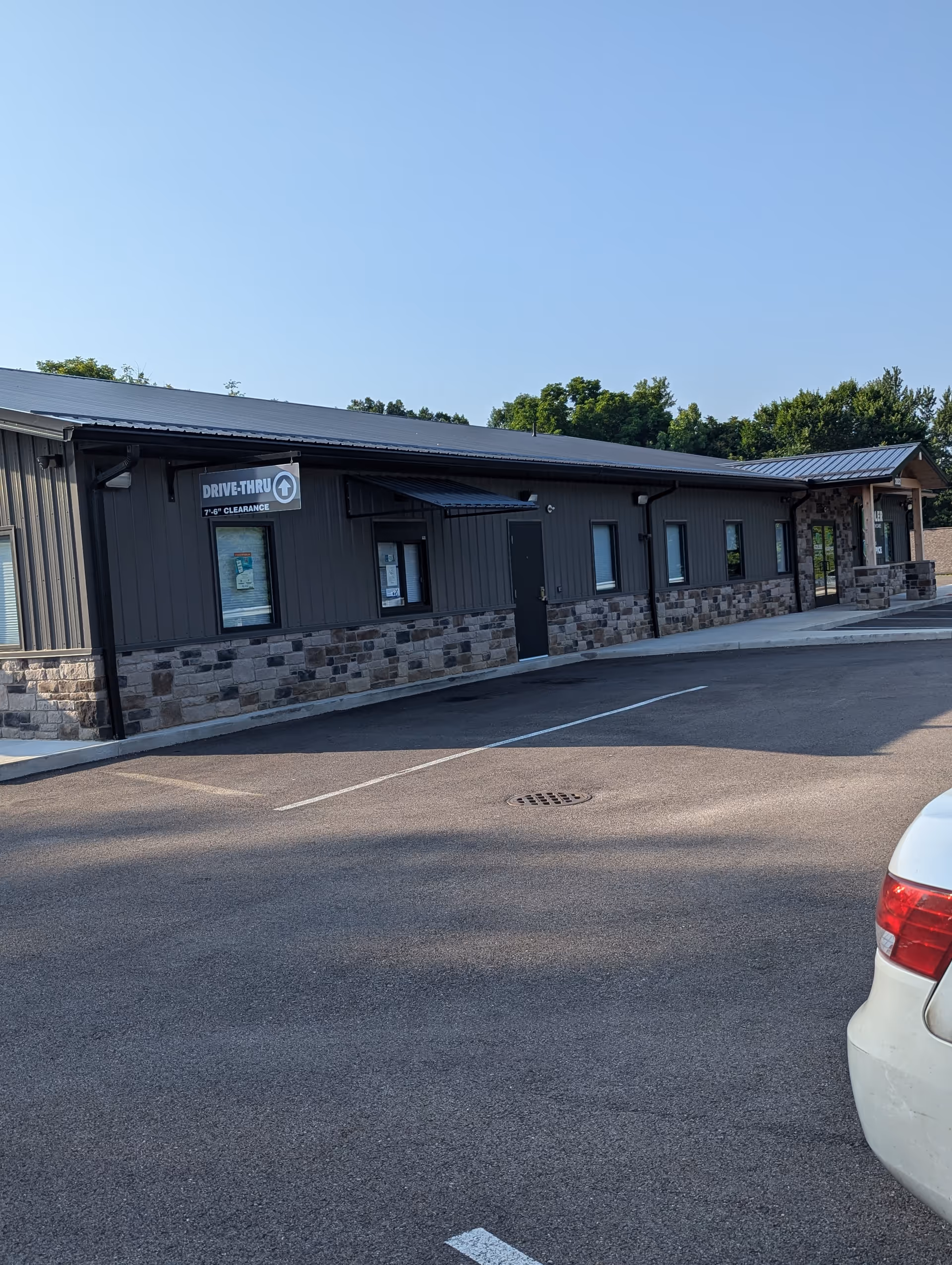 Exterior view of a single-story building with stone veneer and a drive-thru sign.