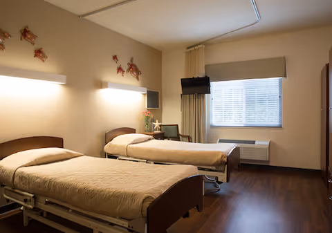 Shared hospital-style bedroom with two single beds, wood floor, and a window