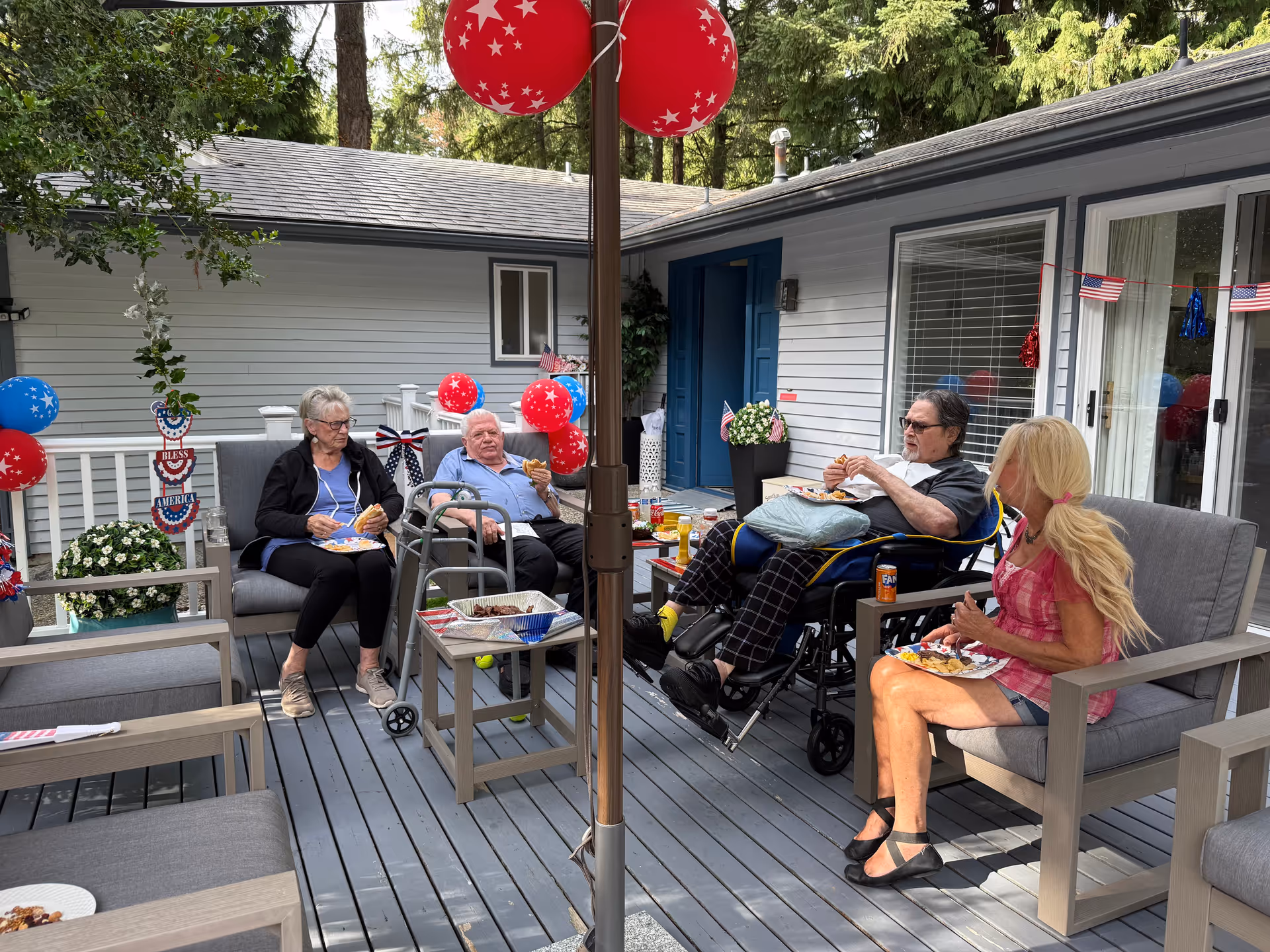 Residents and a caregiver enjoy snacks on a decorated outdoor patio with balloons.