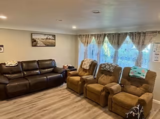Living room with brown sofa, three recliners, curtains, framed art.