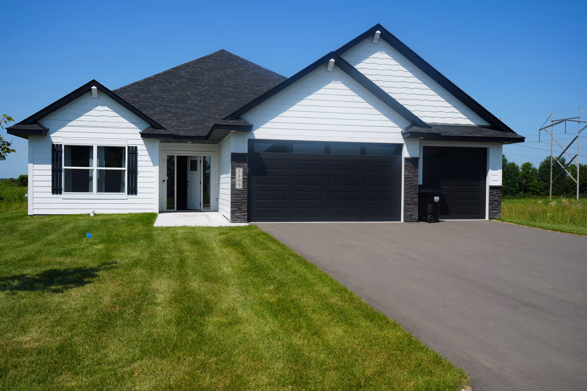 White modern single-story home with a dark three-car garage, green lawn, and paved driveway.