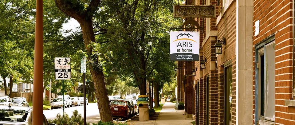 Brick senior living facility on a tree-lined street with ARIS at home signage.