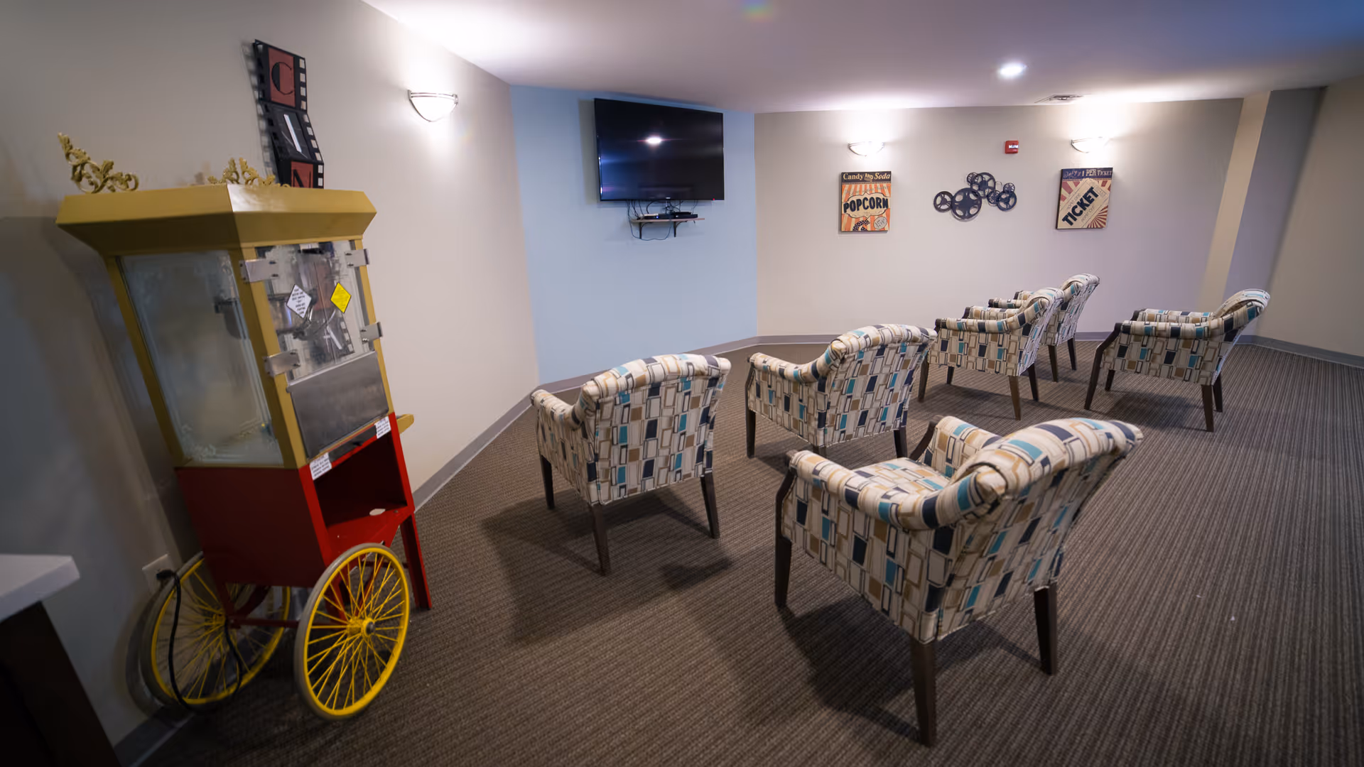 A lounge area with patterned armchairs, a popcorn cart, and a wall-mounted TV.