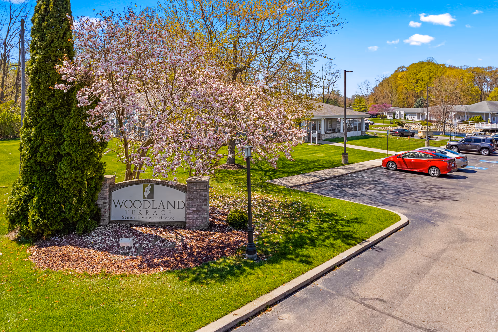 Exterior view of Woodland Terrace sign with blooming trees and a parking lot