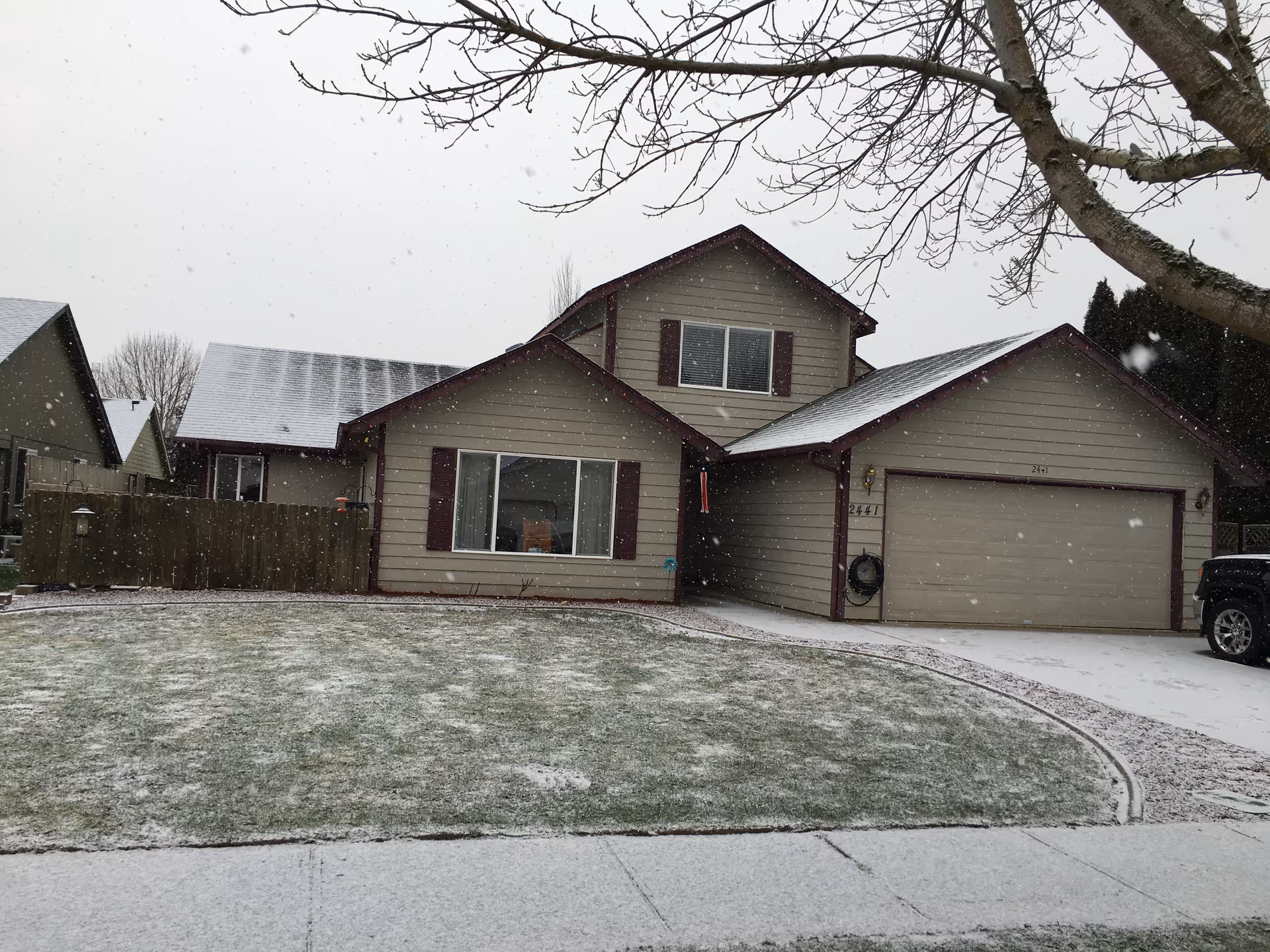 Front view of a beige two-car garage house in a snowy suburban yard.