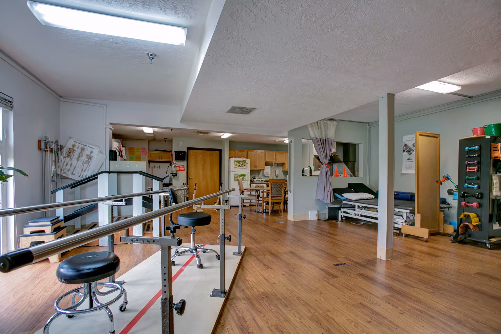 A rehabilitation gym inside a senior facility with parallel bars, mats, and exercise equipment.