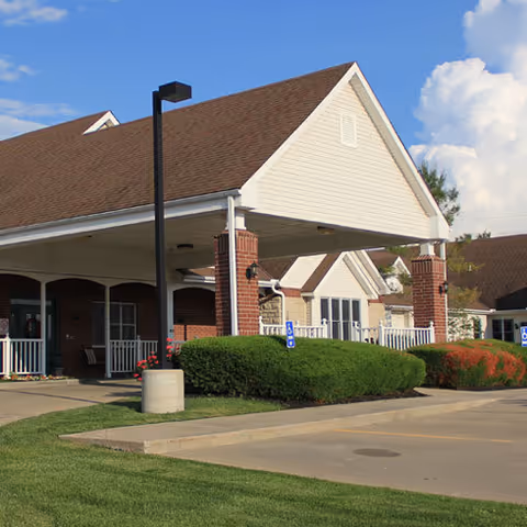 Front exterior of Vintage Park at Gardner with covered entrance, brick columns, and landscaped shrubs.