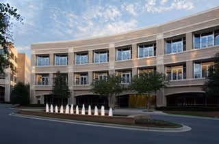 Curved, multi-story senior living facility exterior with glass windows, trees, and a circular driveway.